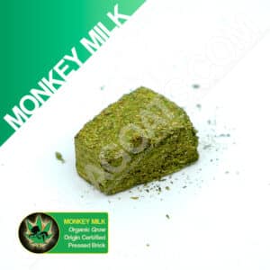 Close up photo of the pressed brick cannabis strain Monkey Milk. Text next to the flower states the name of the strain, that it is organically grown, and pressed brick weed.